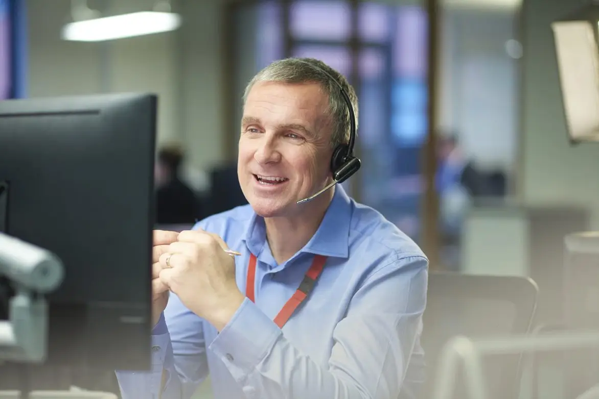 Man with a headset smiling during a conversation in an office environment.
